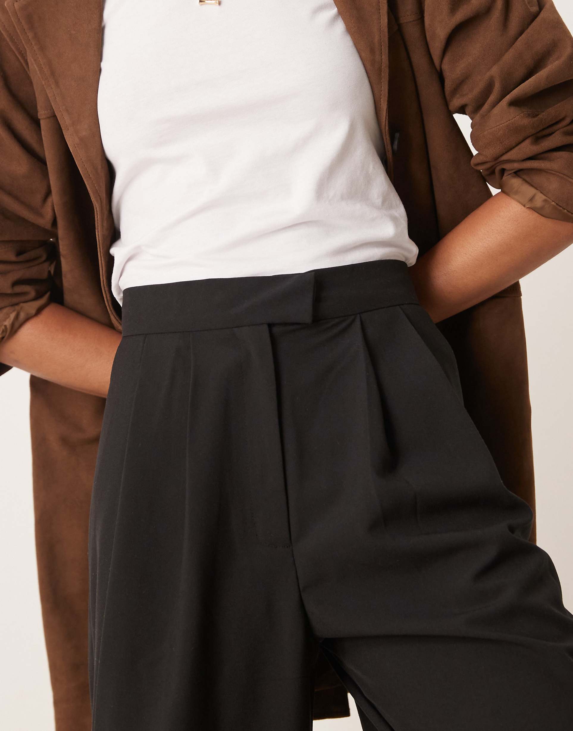 Person wearing a brown coat, white shirt, and black pants on a plain background