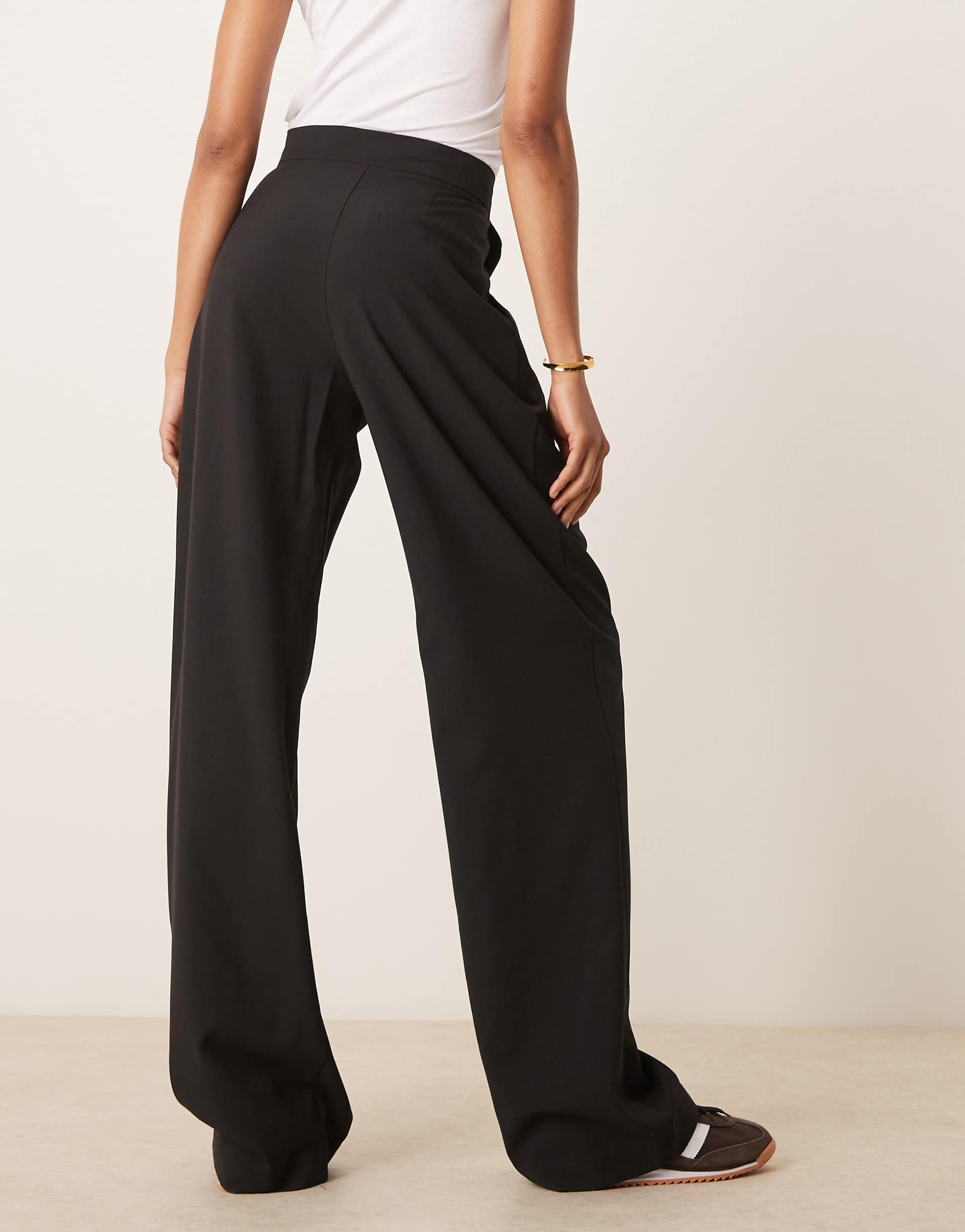 Person wearing black wide-leg pants and a white top on a plain background