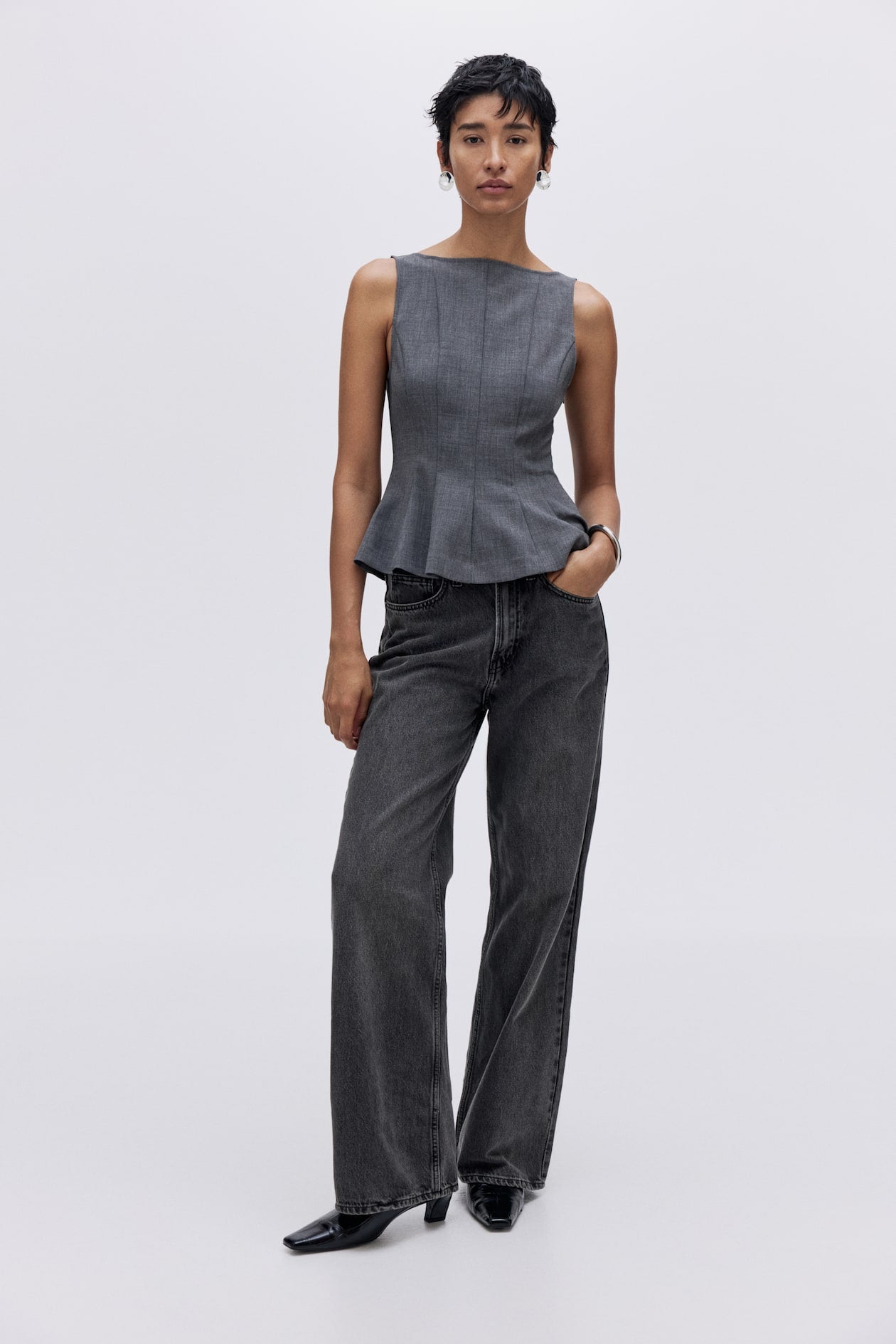Person wearing a gray peplum top and wide-leg jeans on a white background