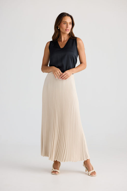 Woman wearing a black sleeveless top and beige pleated skirt on a white background