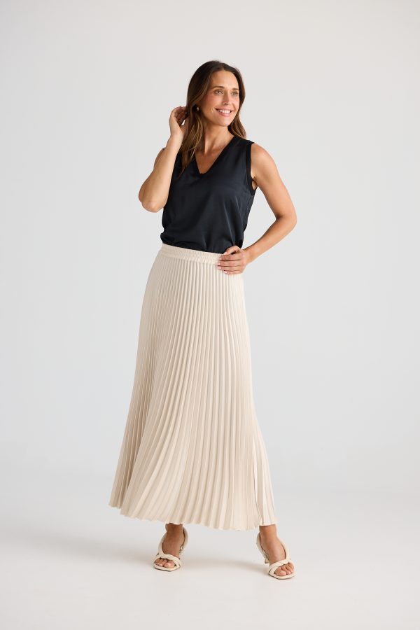 Woman wearing a black sleeveless top and beige pleated skirt on a white background