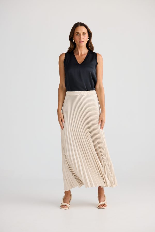 Woman wearing a black sleeveless top and beige pleated skirt on a white background