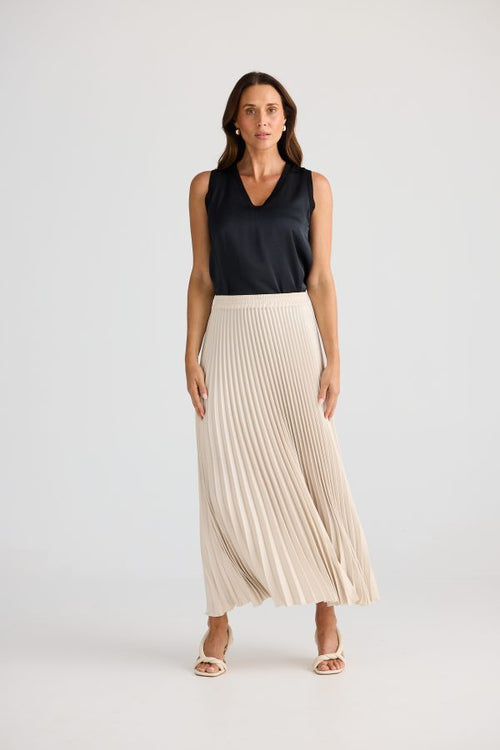 Woman wearing a black sleeveless top and beige pleated skirt on a white background