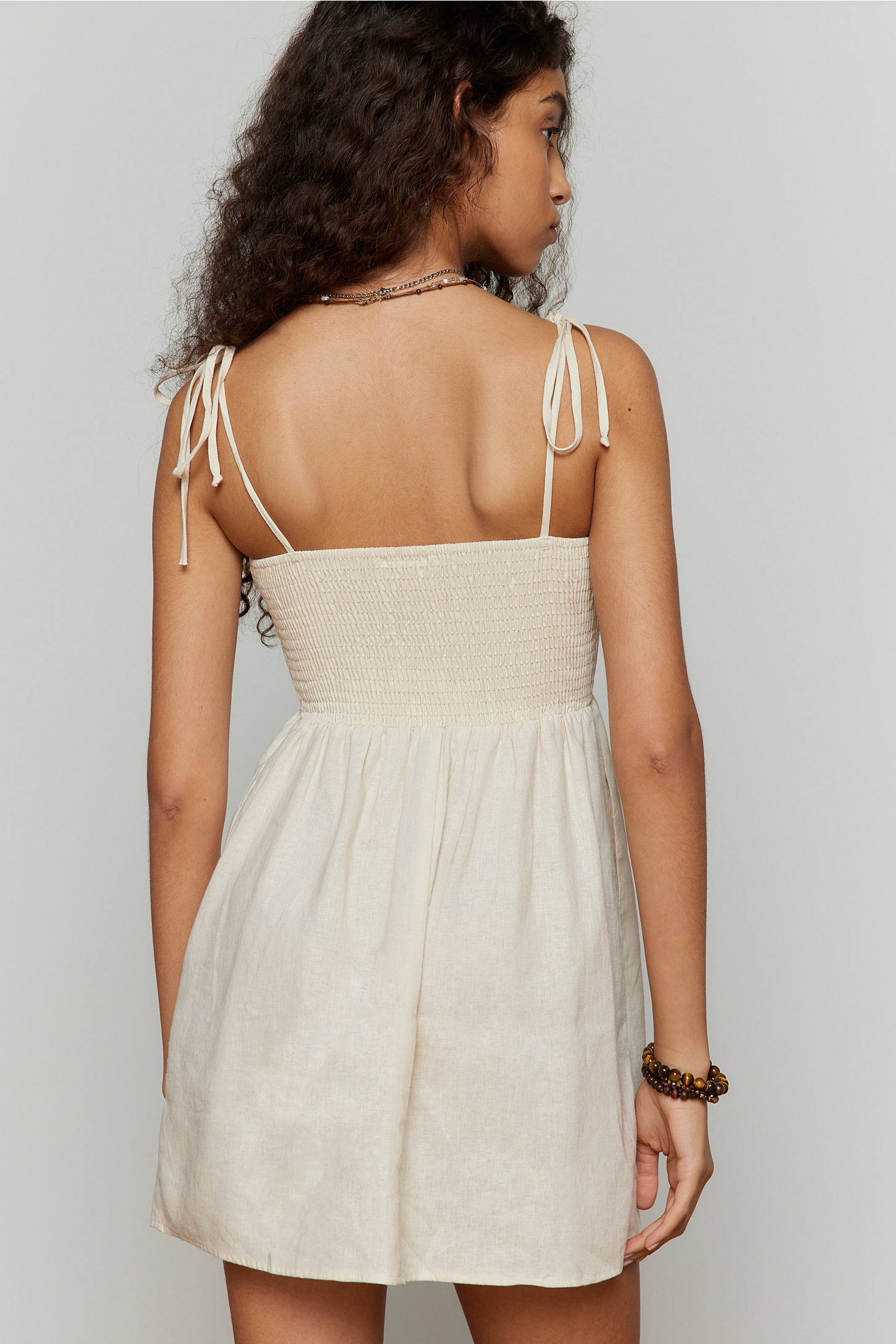 Woman wearing a beige dress with thin straps against a plain background