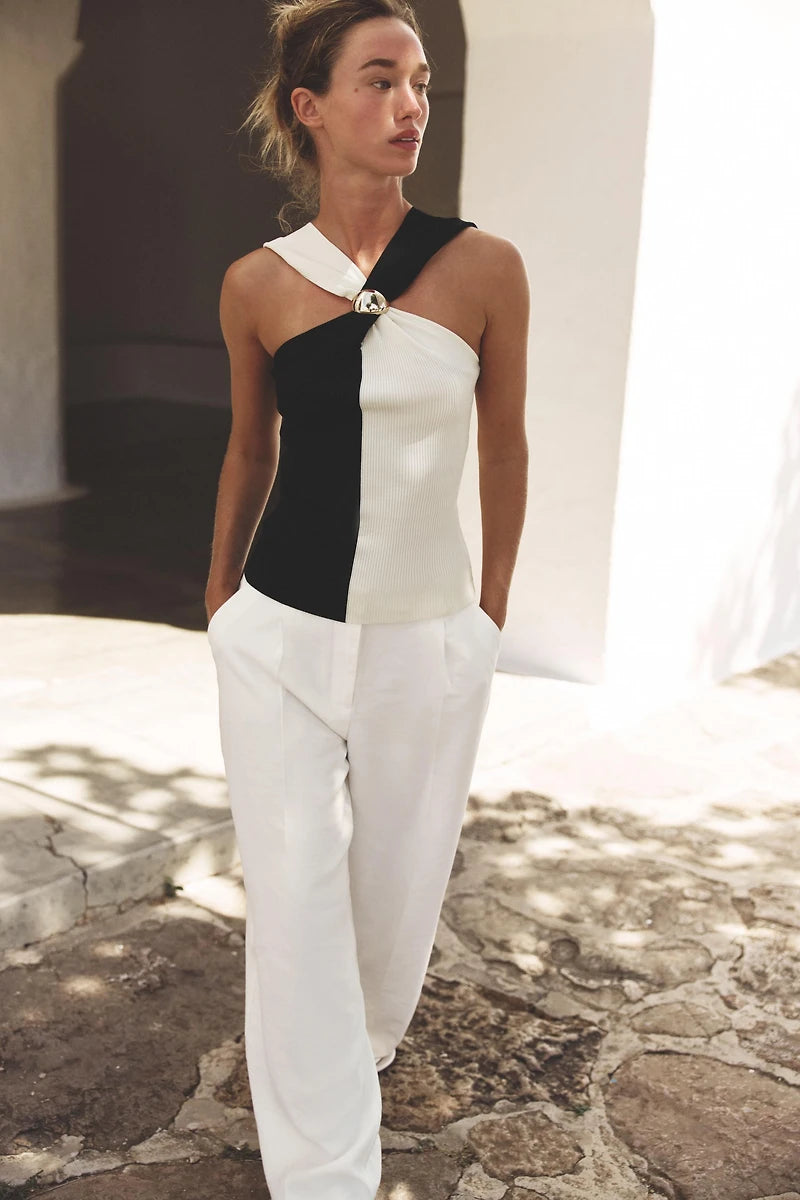 Woman wearing a black and white halter top with white pants standing outdoors.